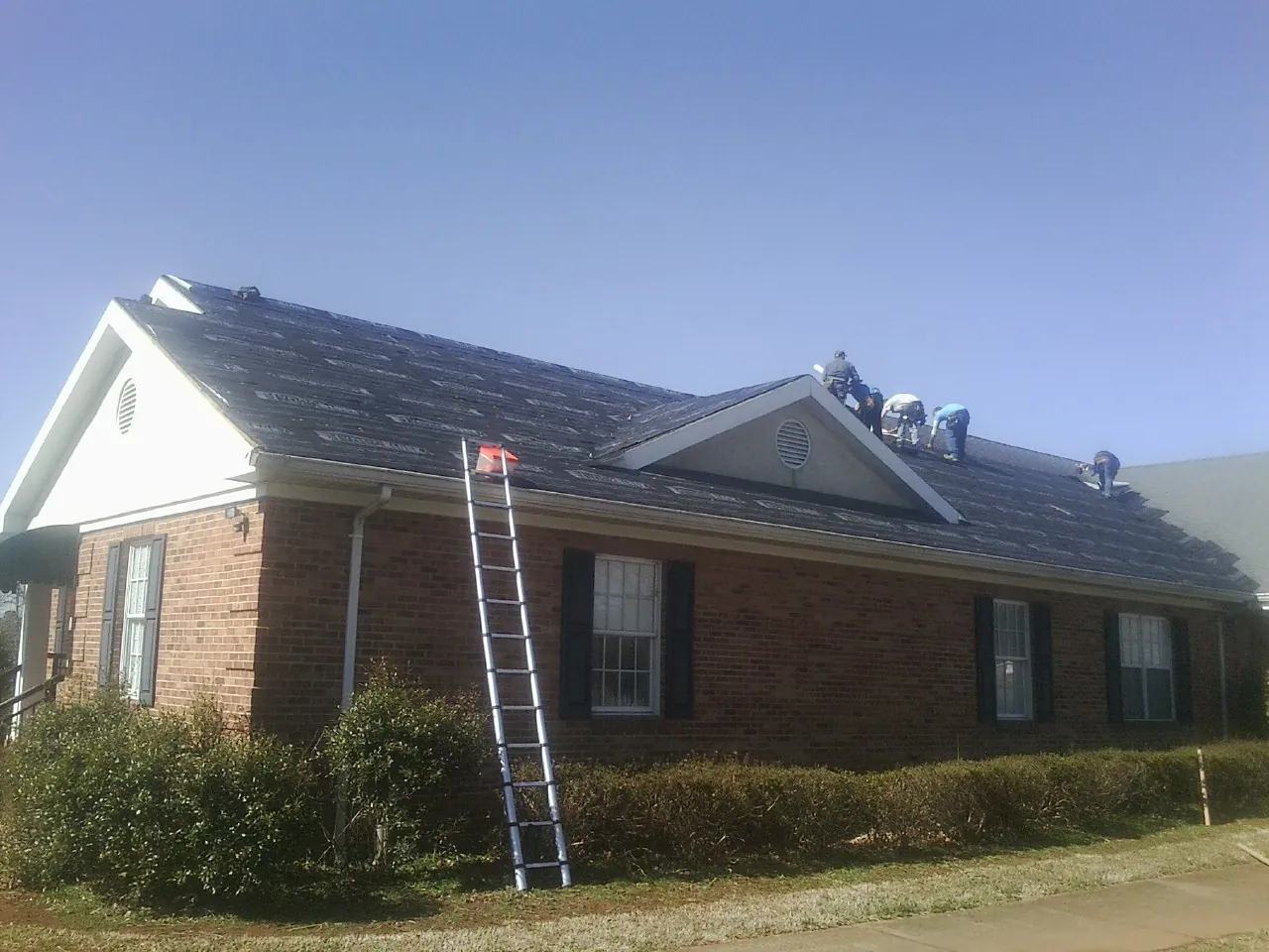 Crew tearing shingles off a brick ranch roof with a ladder set — Metal Roof Repair work by our crew in College Springs