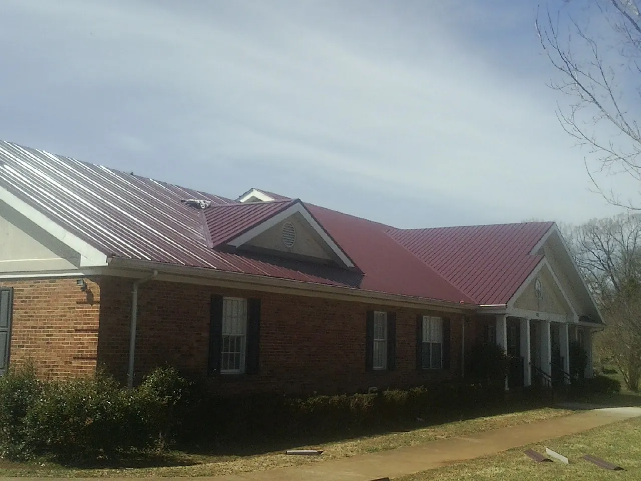 Red metal roof with gabled entries on a long brick building, from a Hail Damage Roof Repair job in College Springs