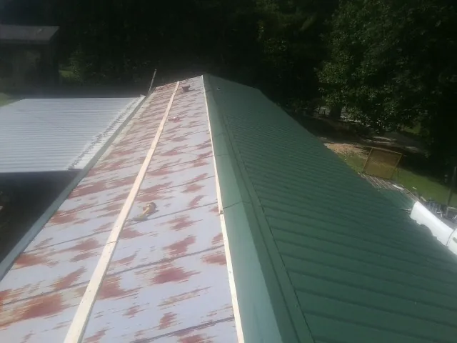 Old rusted panels beside newly installed green metal roofing — Wind Damage Roof Repair by Roofing Brothers in College Springs
