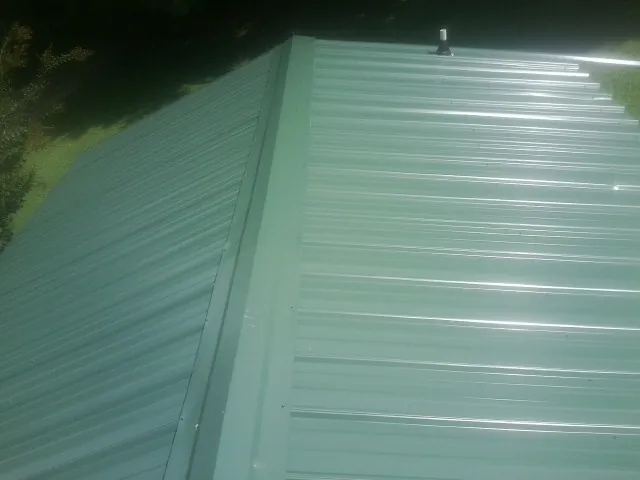 New green metal panels meeting at the ridge of a roof — Flat Roof Repair work by our crew in College Springs