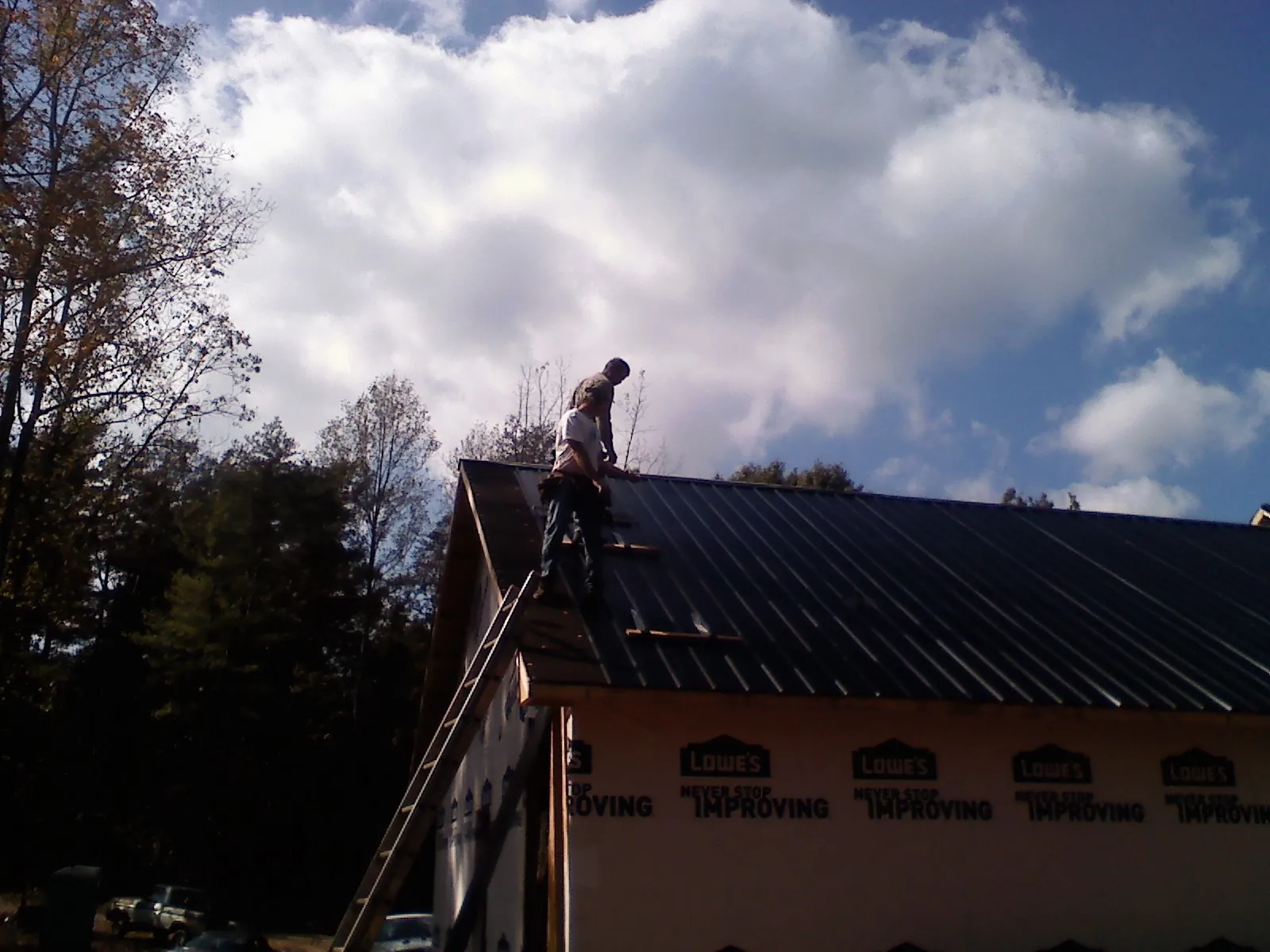 Roofer fastening dark metal panels high against a cloudy sky, from a Roof Inspection job in College Springs
