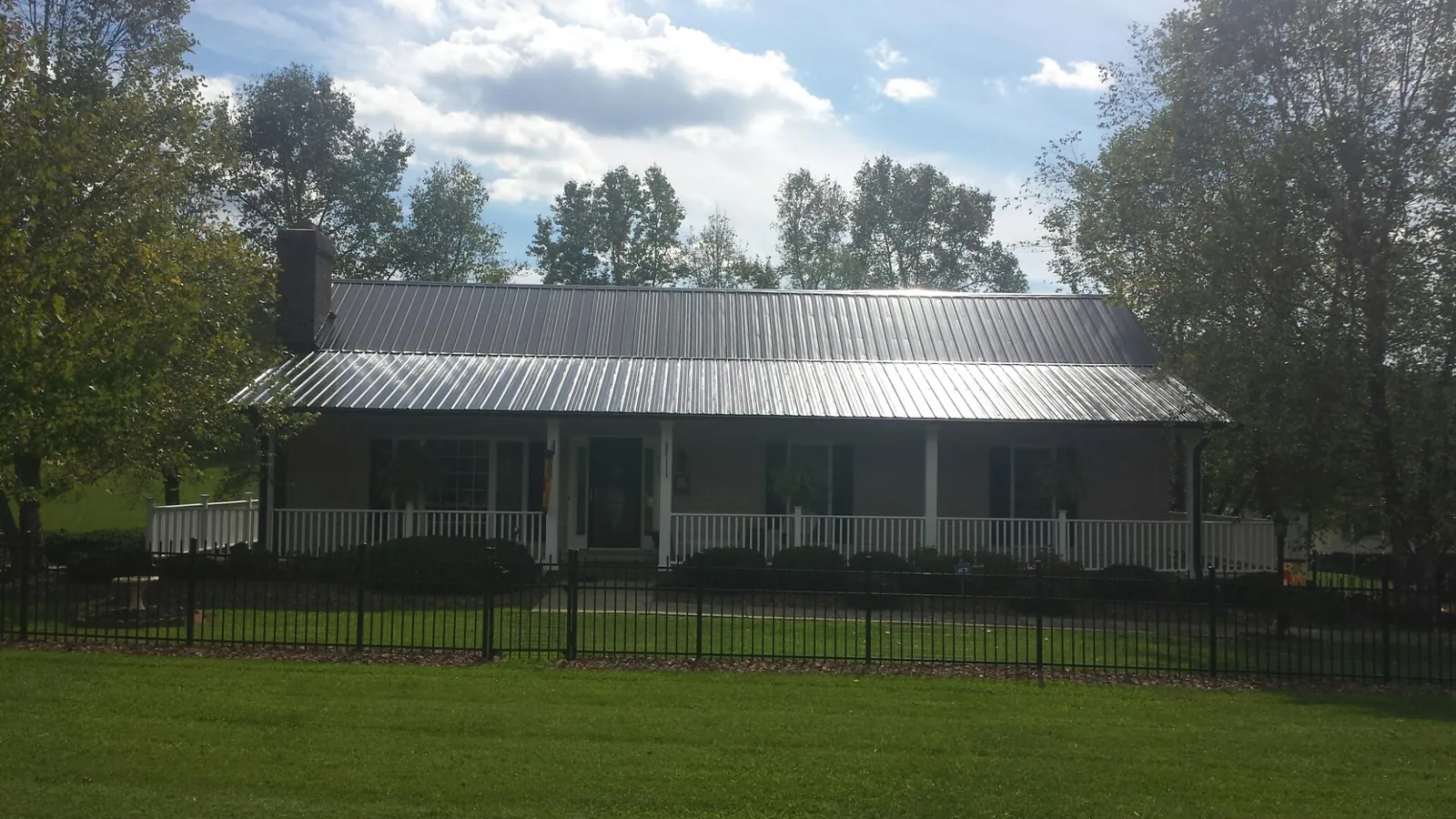 Gray metal roof on a brick ranch with a full width front porch — Gutter Guard Installation work by our crew in College Springs