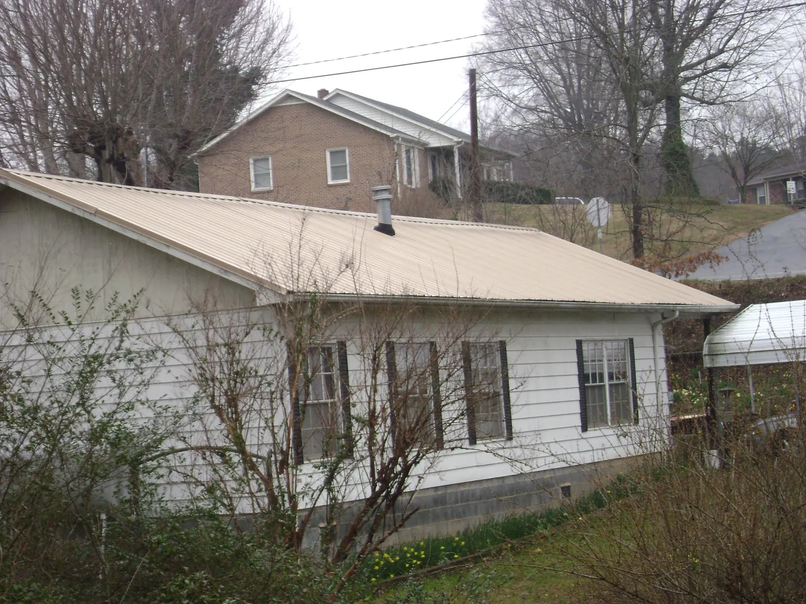 Tan metal roof on a white sided house set into a hillside — Commercial Roofing by Roofing Brothers in College Springs