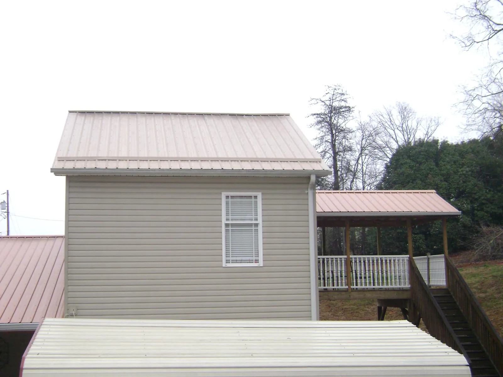 Tan metal roofs on a two story addition and attached porch, from a Roof Replacement job in College Springs
